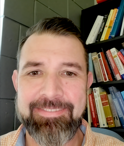 a man smiling next to a book shelf
